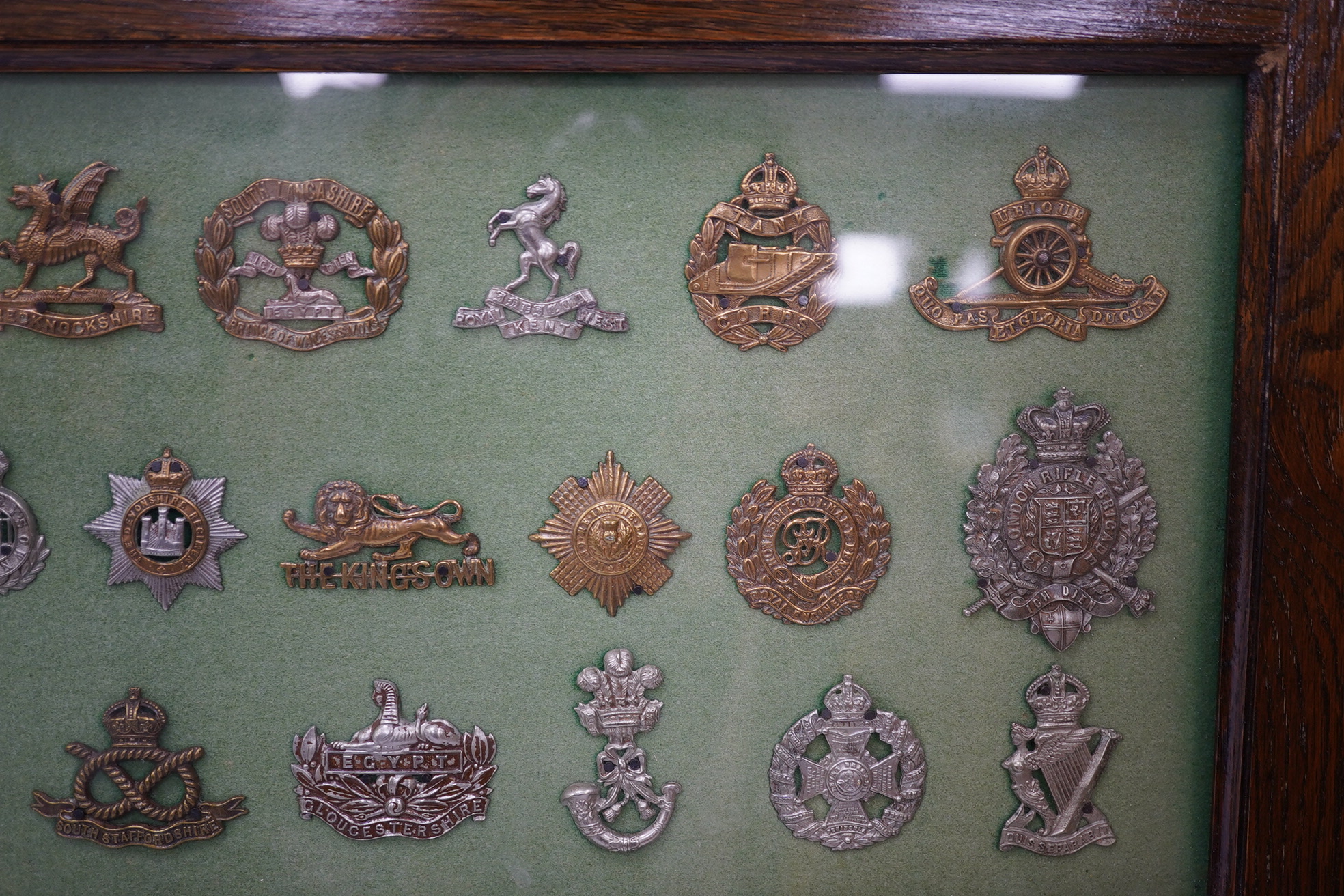 An oak framed display case of cap badges from the British, Colonial and Dominion Regiments, forty-nine badges including Australian Commonwealth Military Forces, the Royal Warwickshire Regiment, the Wiltshire Regiment, th